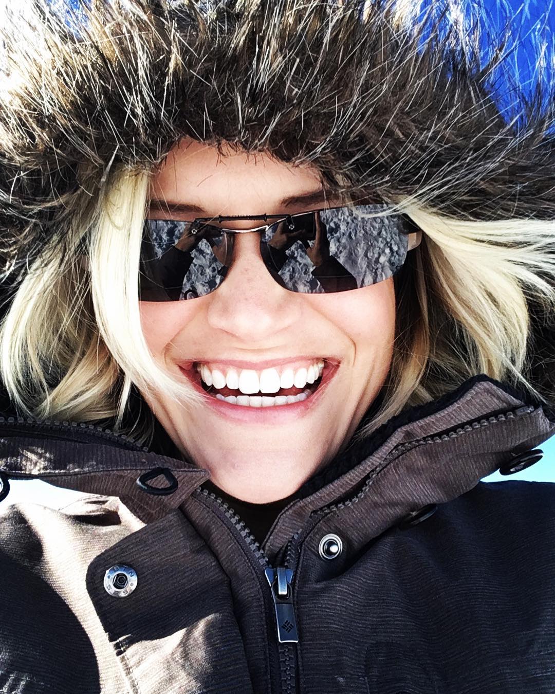 young woman smiling at you all bundled up wearing a warm winter coat